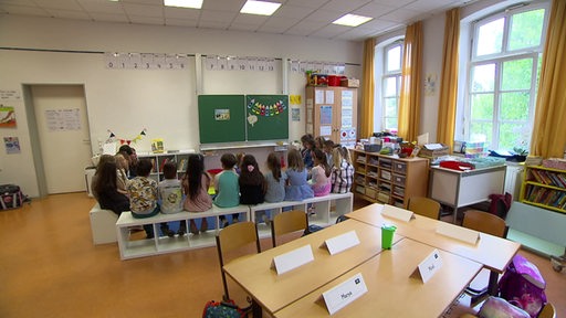 Eine Klasse sitzt bei ihrem ersten Schultag in einem Sitzkreis vor einer Tafel.
