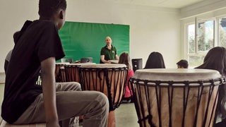 Kinder sitzen in einem Klassenzimmer an Trommeln.