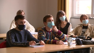 Mehrere Abiturienten sitzen im Klassenraum mit Masken. 