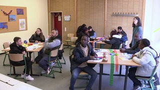 Mehrere Personen sitzen in einem Klassenraum an den Tischen.