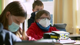 Schüler und Schülerinnen in ihrem Klassenraum beim lernen während der Corona-Pandemie mit Masken.