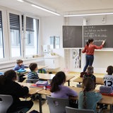 Eine Frau steht neben einer Tafel und unterrichtet Kinder.