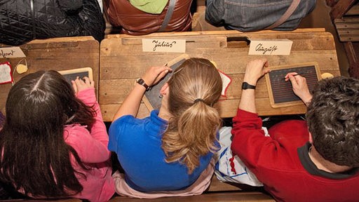 Kinder sitzen im Schulmuseum auf alten Schulbänken und schreiben auf Tafeln