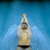 Ein Mann mit Badekappe und Schwimmbrille schwimmt auf dem Rücken durch ein Wasserbecken.