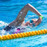 Eine junge Triathletin schwimmt im Kraulstil im Schwimmbad, mit hohem Ellbogen holt sie den Arm zurück nach vorne und atmet dabei ein.