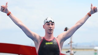 Schwimm-Star Florian Wellbrock reckt nach seinem WM-Sieg im Freiwasser auf dem Podium die Arme triumphierend hoch.