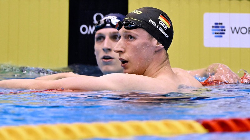 Schwimm-Star Florian Wellbrock schaut im Becken enttäuscht auf die Anzeigetafel nach seinem 800-Meter-Vorlauf. Neben ihm Schwimmer Lukas Märtens.