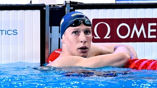 Schwimm-Olympiasieger schaut nach einem WM-Vorlauf im Becken gebannt auf die Anzeigetafel mit den Zeiten.