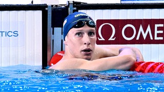 Schwimm-Olympiasieger schaut nach einem WM-Vorlauf im Becken gebannt auf die Anzeigetafel mit den Zeiten.