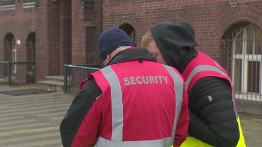 Mitarbeiter eines Sicherheitsdienstes stehen vor einer Bremerhavener Schule