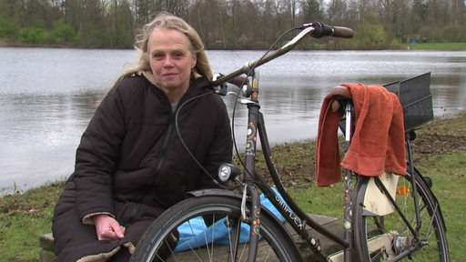 Die Eisbaderin und Künstlerin Silke Rosenthal sitzt neben ihrem Fahrrad an einem See.