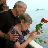 Eine Frau steht auf einem Schiff und wirft Rosen ins Meer, ein Mann hat den Arm um sie gelegt.