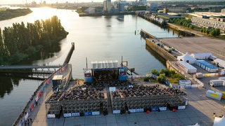 Luftaufnahme einer Open-Air-Bühne mit vollbesetztem Auditorium an einem Hafenbecken