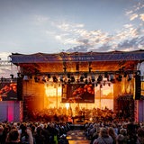 Konzert vor viel Publikum auf großer Open-Air-Bühne bei Sonnenuntergang