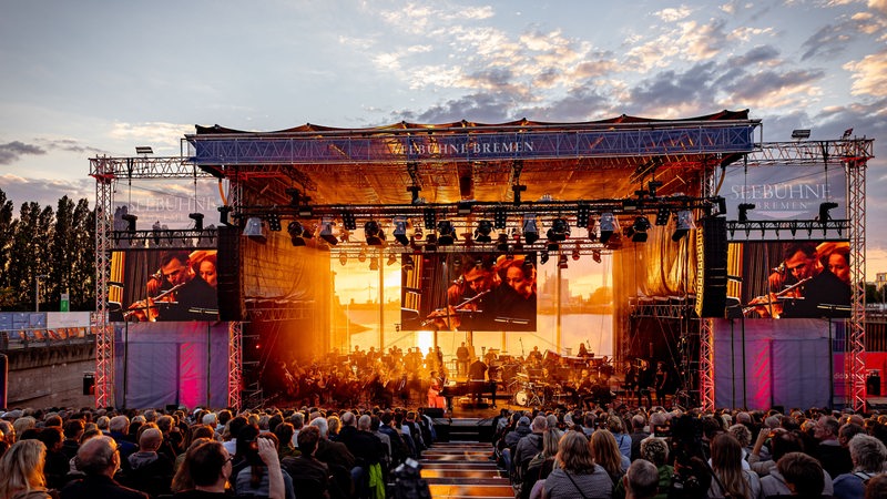 Konzert vor viel Publikum auf großer Open-Air-Bühne bei Sonnenuntergang