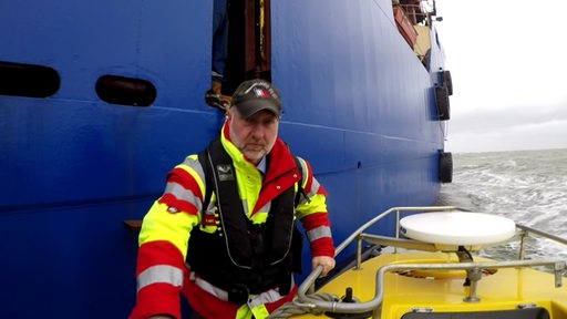 Ein Seelotse steigt auf dem Meer von einem großen Schiff auf ein Beiboot.