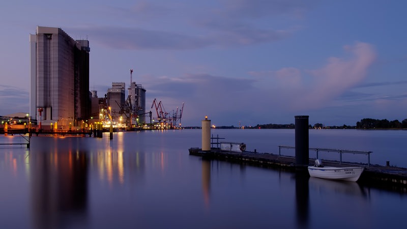 Der Hafen in Brake ist während der Abenddämmerung zu sehen. Im Vordergrund liegt ein kleines Ruderboot an einem Steg.