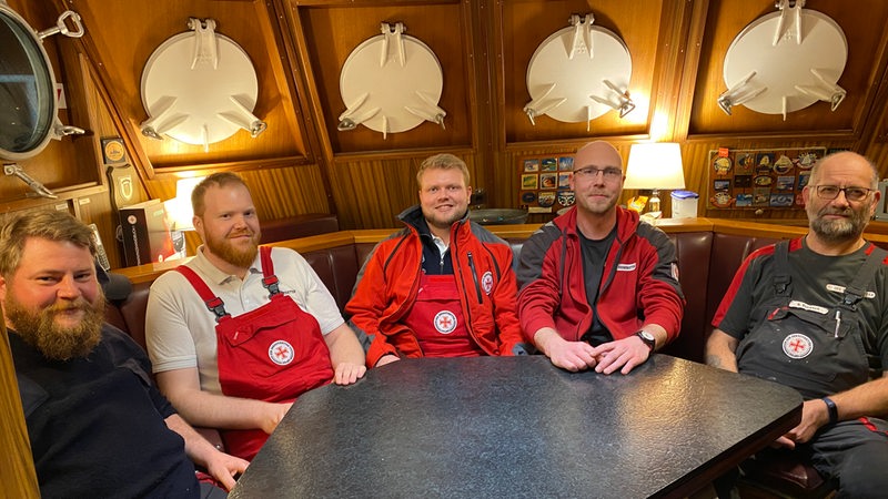 Die Crew eines Seenotretters aus Bremerhaven sitzt um einen Tisch verteilt.