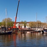 Ein Hafen, am Festland steht ein Kran; mehrere Männer auf bergen ein Boot.