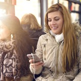 Eine junge Frau sitzt mit Kopfhörern und Smartphone in einer Straßenbahn