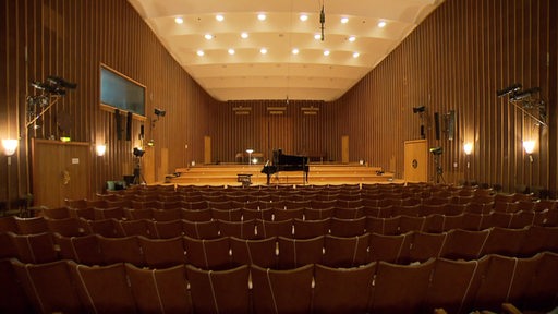 Der Sendesaal aus einer leeren Zuschauerreihe aus aufgenommen. Am Rand stehen Mikrofone und auf der Bühne ein Flügel.