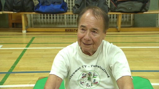 Der Seniore Willy Wege auf der Sportmatte in einer Sporthalle. 