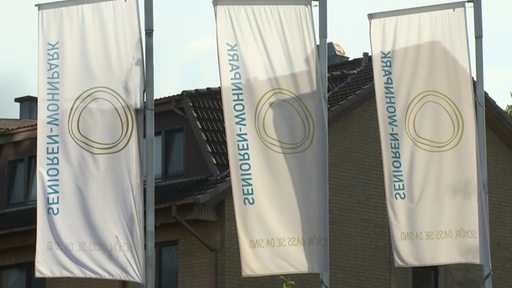 Drei Flaggen wehen im Wind. Sie zeigen das Logo des Senioren-Wohnparks Langen.