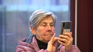 Eine ältere Frau schaut auf ihr Smartphone und tippt etwas ein.
