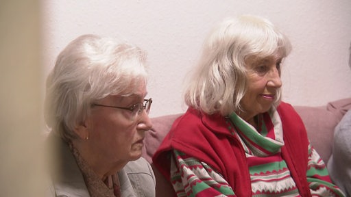 Zwei Seniorinnen sitzen auf einer Couch im Pflegeheim. 