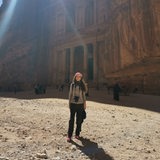 Eine Frau steht mit Spiegelreflexkamera vor einem Felsgebäude in Petra.