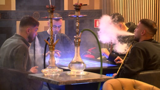 Mehrere junge Menschen sitzen in einer Shisha Bar und rauchen Shisha.