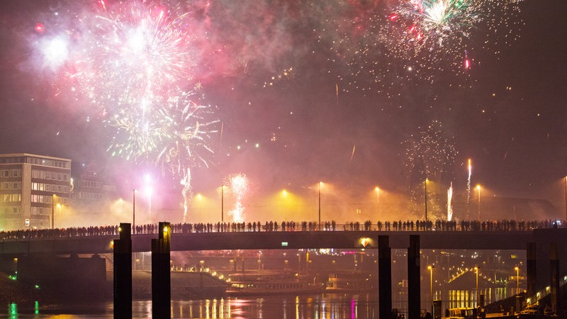 Menschen stehen auf einer Brücke in Bremen und beobachten das Feuerwerk.
