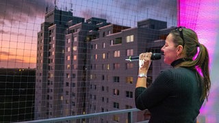 Eine Sängerin mit Mikrofon steht auf einem beleuchteten Balkon bei Nacht