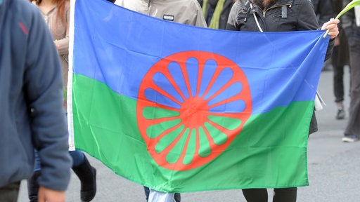 Menschen halten die Flagge der Sinti und Roma während einer Feierlichkeit auf der Straße (Archivbild)