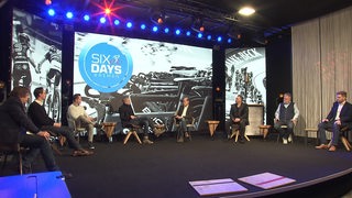 Die Veranstaler der Six Days Bremen sitzen auf der Bühne und reden. 