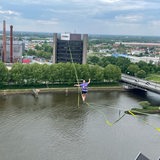 Eine Person hockt hoch oben auf einer Slackline über der Weser