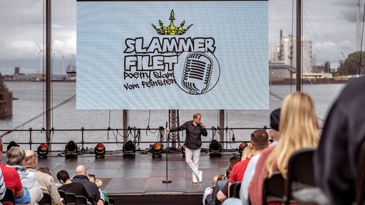 Mann auf Bühne vor Schriftzug "Slammer Filet" vor großem Publikum