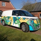 Ein bunter Kleinbus steht vor ländlichen Gebäuden.
