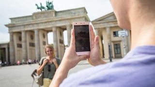 Jemand macht ein Handyfoto von einer Frau vorm Brandenburger Tor