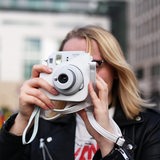 Eine junge Frau fotografiert vor Gebäuden mit einer Sofortbildkamera.