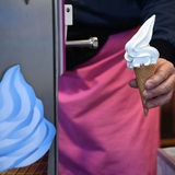 Ein Verkäufer hält ein Softeis an einem Eisstand in die Kamera.