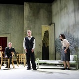 Foto von einer Szene im Theater mit sechs Männern und Frauen im Vordergrund einer angedeuteten Wohnung