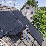 Ein Mann bei der Installation einer Solar und Photovoltankikanlage auf dem Dach eines Einfamilienhaus 