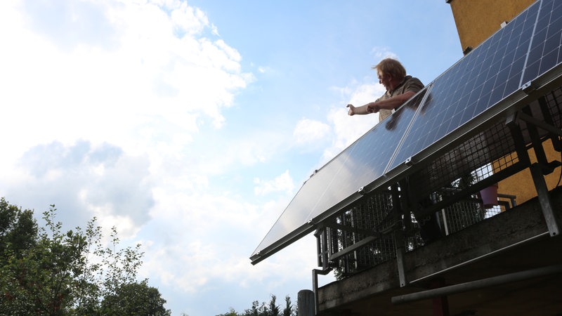 Ein Mann steht auf einem Balkon neben einer Solarplatte für die Stromgewinnung.