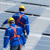 Zwei Techniker in Arbeitskleidung gehen zwischen Solarpanelen