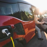 Eine Frau steigt bei sonnigen Wetter aus ihrem E-Auto aus, was gerade aufgeladen wird.