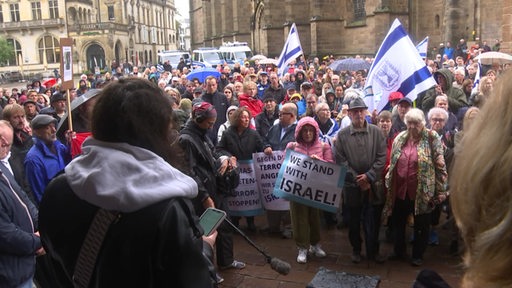In der Bremer Innenstadt stehen mehrere Menschen mit Plakaten und israelischen Fahnen bei einer Solidaritätskundgebung.
