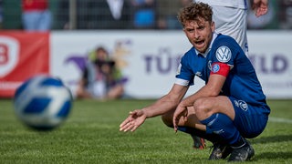 Der Kapitän des Bremer SV sitzt auf dem Spielfeld in der Hocke und schimpft über eine Entscheidung.