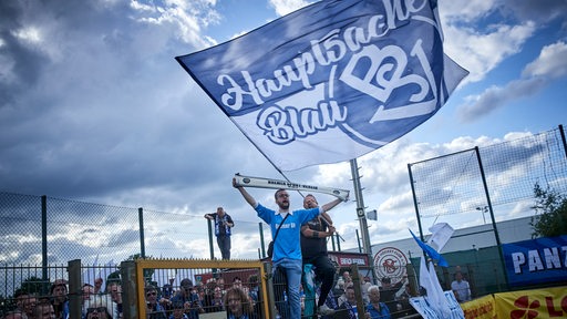 Fans des Bremer SV feiern den Pokal-Sieg ihrer Mannschaft auf dem Zaun mit einer großen blau-weißen Fahne.