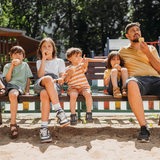 Familie sitzt mit einer Kugel Eis draußen auf einer Parkbank.